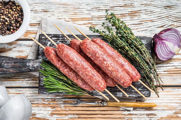 Salsichas de carne kofta ou lula kebabs crus em espetos com ervas. fundo de madeira escuro. vista do topo.