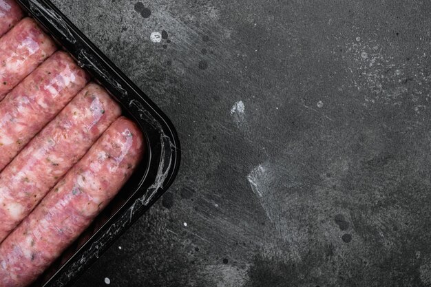 Salsichas de carne não cozidas em pacote de plástico em fundo de mesa de pedra escura preta vista superior plana com espaço de cópia para texto