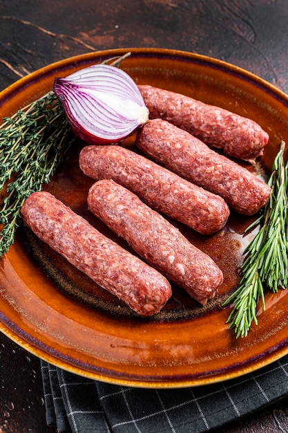 Salsichas de espetadas de carne kofta crua em um prato com ervas. Fundo escuro. Vista do topo.