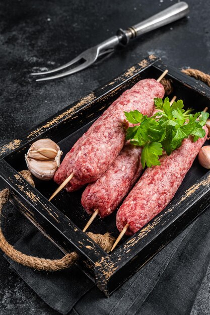 Salsichas de kebabs de carne crua fresca em espetos em bandeja de madeira Fundo preto Vista superior