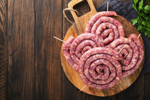 Salsichas de porco em espiral cruas Salsichas de porco frescas saborosas espirais torcidas para churrasco no carrinho branco com especiarias e ervas para jantar de festa de Octoberfest em fundo de madeira velho Vista superior Conjunto de Oktoberfest