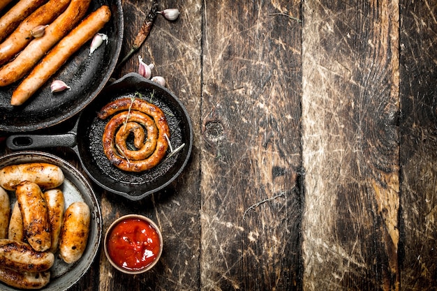 Salsichas diferentes em panelas com molho de tomate na mesa de madeira.