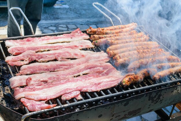 Salsichas e bacon cozinhando no churrasco de fumar no terraço