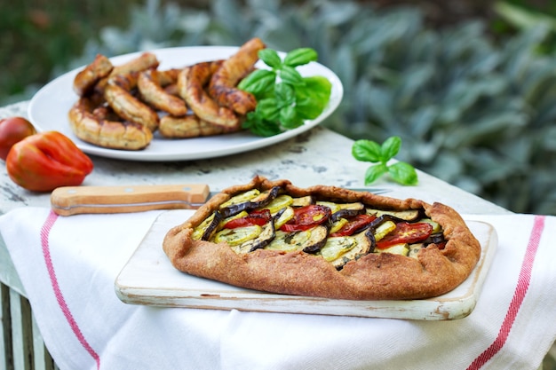 Salsichas e tortas vegetarianas com legumes e ervas em uma mesa de madeira no jardim.