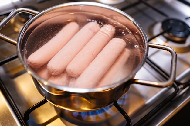 Salsichas em água fervente em uma panela no queimador do fogão a gás preparação de produtos semi-acabados para almoço refeições simples para todos os dias