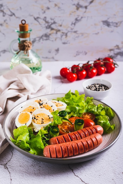 Foto salsichas fritas tomates alface e um sanduíche com um ovo cozido em um prato vista vertical
