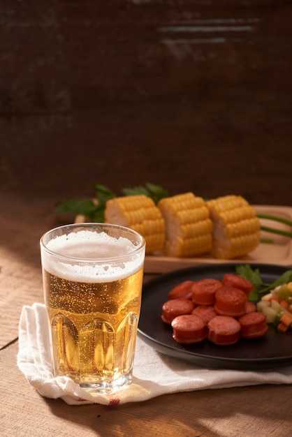 Salsichas grelhadas com copo de cerveja na mesa de madeira com espaço de cópia.