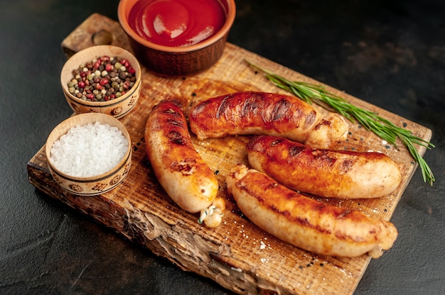 Salsichas grelhadas com especiarias, ketchup e alecrim em uma mesa de pedra, pronta para comer