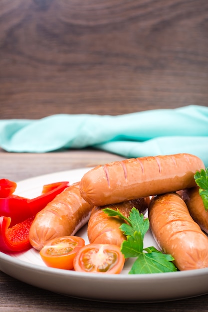 Salsichas grelhadas com legumes em um prato sobre uma mesa de madeira