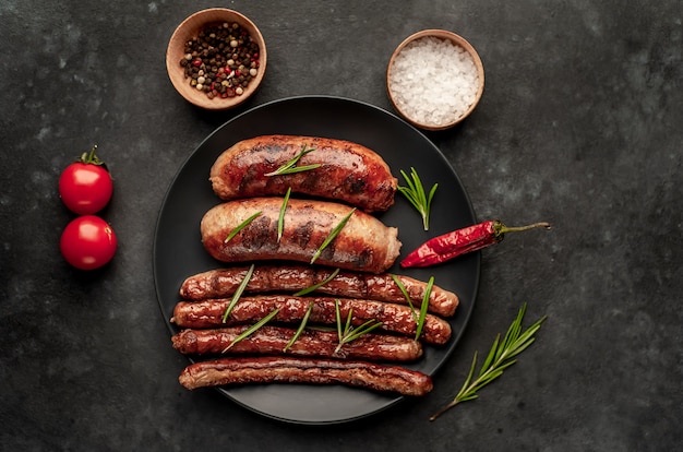 salsichas grelhadas diferentes em um prato escuro com especiarias e alecrim, em uma mesa de pedra, pronta para comer