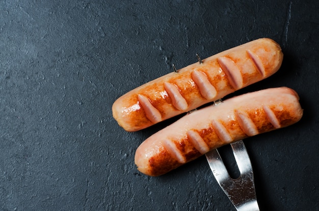 Salsichas grelhadas fritas em um garfo de metal. dieta não saudável.