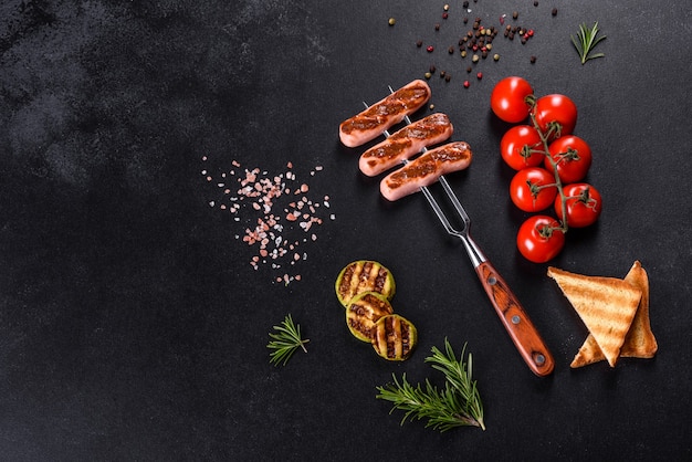 Salsichas saborosas e frescas grelhadas com vegetais, especiarias e ervas. Foto do prato acabado em uma mesa de concreto escura