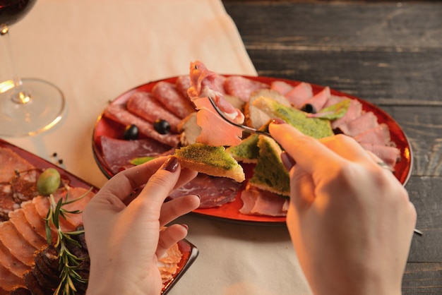 Salsichas sortidas, jamon e presunto com fatias de pão frito num prato vermelho. Em uma mesa de madeira