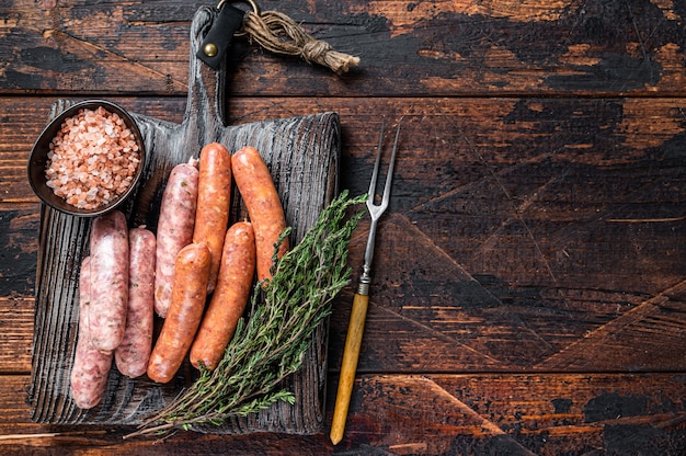 Salsichas variadas de porco cru e bovino com especiarias em uma placa de madeira com tomilho