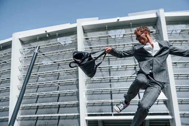 Saltando e comemorando o sucesso Jovem empresário com roupa formal cinza está ao ar livre na cidade