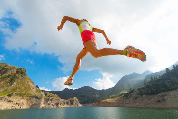 Foto saltando niña mientras corre cerca de un lago de montaña