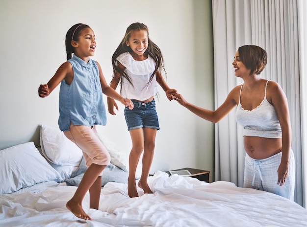 Saltando Toma de una alegre familia joven saltando en una cama juntos en casa durante el día