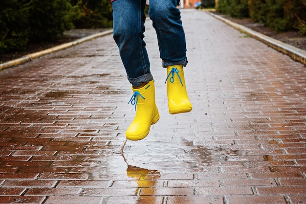 Saltar en el charco Piernas femeninas en botas de goma amarillas saltando en el charco Mujer joven despreocupada en botas de lluvia salta