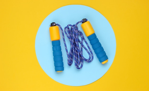 Saltar la cuerda sobre fondo amarillo con círculo azul pastel en el medio. Vista superior. Concepto de deporte minimalista.