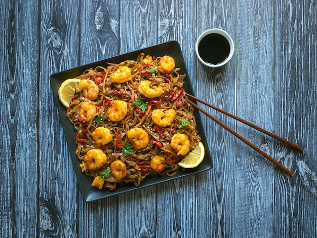 Salteado de fideos con camarones fritos, verduras y salsa de soja. Mesa de comida asiática.