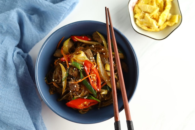 Salteado de fideos de vidrio coreano Japchae servido en el tazón con fondo blanco