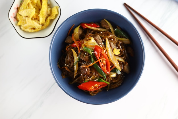 Salteado de fideos de vidrio coreano Japchae servido en el tazón con fondo blanco