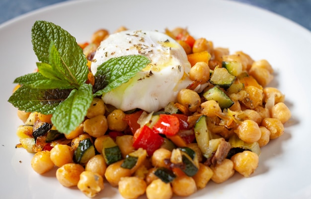 Salteado vegetariano picante casero con garbanzos y dados de pimienta y calabacín con un huevo frito y algo de decoración de menta en un plato blanco. de cerca.