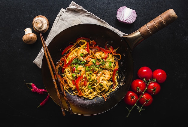 Saltear los fideos en wok chino tradicional, palillos. Ingredientes para cocinar fideos.