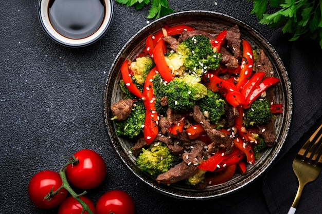 Saltee las verduras con pimentón de ternera y brócoli con semillas de sésamo en un tazón en la vista superior del fondo de la mesa negra