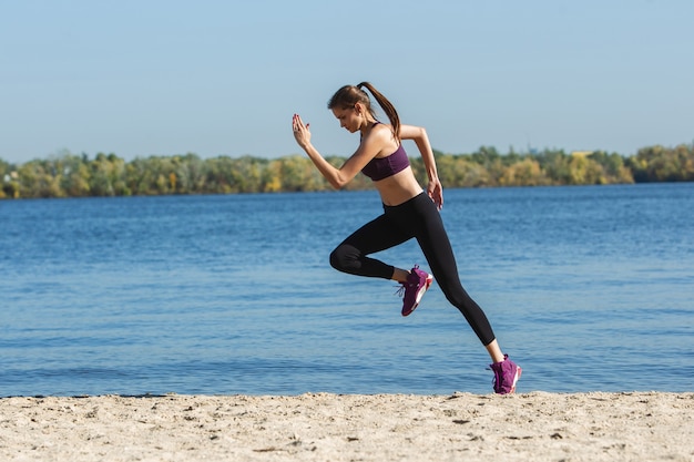 Salto alto. Joven atleta, mujer entrenando, practicando al aire libre bajo el sol de otoño. Hermosa deportista caucásica trabajando al aire libre. Concepto de deporte, estilo de vida saludable, movimiento, actividad.