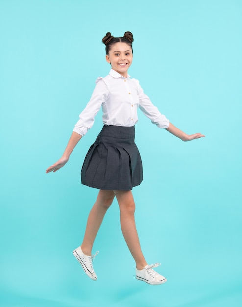 Salto de comprimento total de menina adolescente no estúdio isolado azul usar saia e camisa casuais Menina da escola engraçada espantada gênio da criança excitada jovem estudante Feliz adolescente emoções positivas e sorridentes