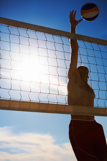 Salto de vôlei e homem na praia com bola serve energia ou liberdade em fundo de céu azul esportes de fitness ou jogador masculino com handebol na natureza para treino de cardio ou desempenho de jogo atlético