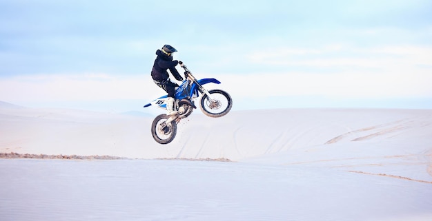 Salto en el desierto o persona que conduce una motocicleta para acción, aventura o fitness con rendimiento o adrenalina. Riesgo de arena o atleta deportivo en motocicleta en dunas para ejercicio de entrenamiento o desafío de carrera.