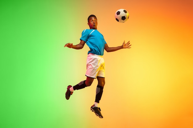 Salto em altura. Futebol masculino, treinamento de jogador de futebol em ação isolado no fundo do estúdio gradiente em luz de néon. Conceito de movimento, ação, realizações, estilo de vida saudável. Cultura jovem.