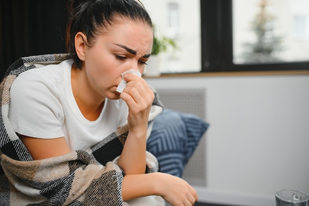Foto salud alergia al frío y concepto de personas mujer enferma sonándose la nariz mocosa en papel tisú en casa