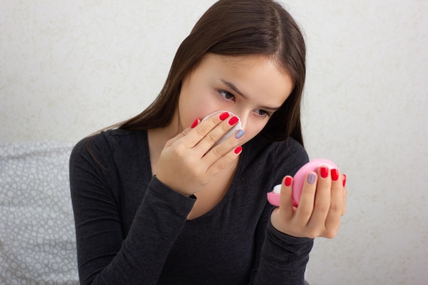 Salud y Belleza. Cuidado de la piel facial. Una niña se frota la cara con una loción tónica y nutritiva.