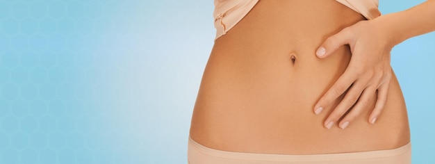 Foto salud, digestión, belleza, personas y concepto de pérdida de peso - cierre de una mujer señalando con el dedo al vientre sobre fondo azul