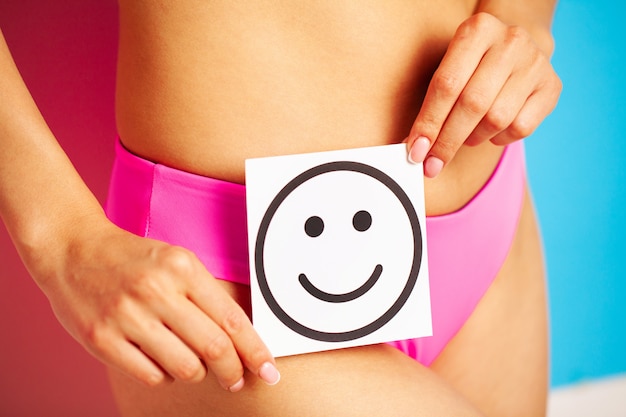 Foto la salud del estómago y los conceptos de buena digestión, cerca de una mujer sana con un hermoso cuerpo delgado en bragas rosas con tarjeta con una sonrisa feliz en las manos.