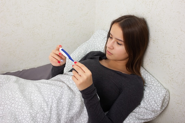 Foto salud y medicina. una niña está enferma en su casa en la cama, sostiene un termómetro.