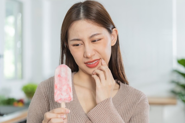 Salud mujer joven asiática tocando la expresión de la mejilla que sufre de dolor de muelas caries o sensibilidad cavidad dientes molares o inflamación comer helado frío en casa Dientes sensibles personas