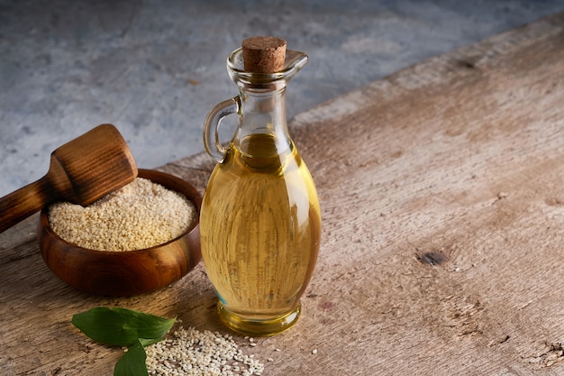 Saludable aceite de sésamo en botella de vidrio y semillas de sésamo en mesa de madera Copia espacio Rústico