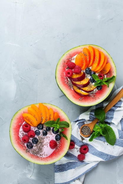 Saludable alimentación limpia dieta y nutrición concepto de desayuno de verano de temporada Ensalada de frutas con yogur en un tazón de sandía tallada en una mesa de cocina Vista superior plano endecha copia espacio fondo