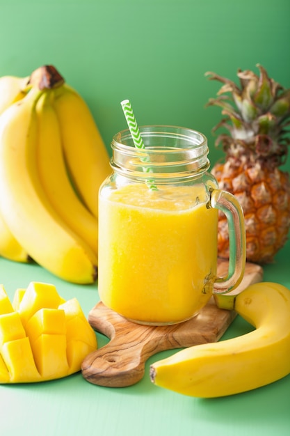 Saludable batido amarillo con mango piña plátano en tarros de cristal