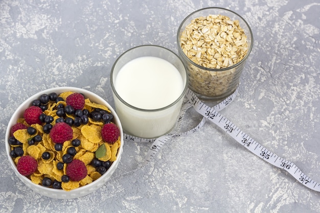 Saludable desayuno sabroso con copos de maíz y bayas, un vaso de leche y un vaso de avena.