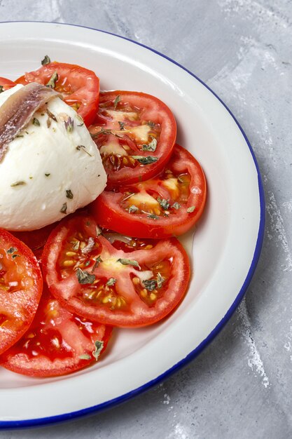 Saludable ensalada casera de tomate con mozzarella, anchoas y orégano