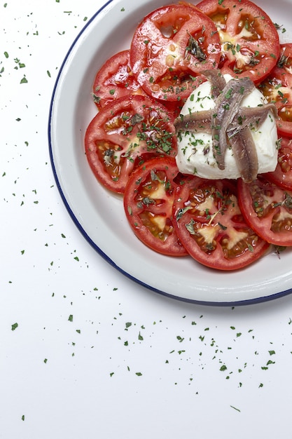 Saludable ensalada casera de tomate con mozzarella, anchoas y orégano