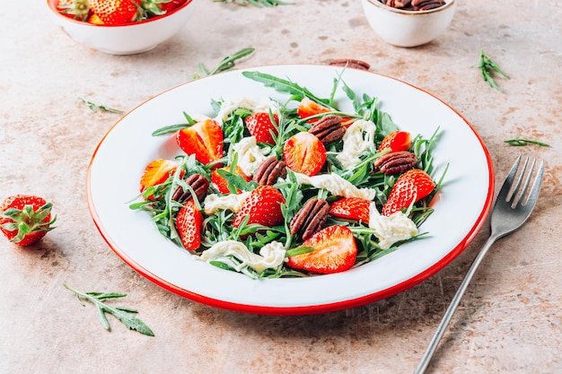 Saludable ensalada de verano con fresas, rúcula, stracciatella y nueces en un fondo rústico beige