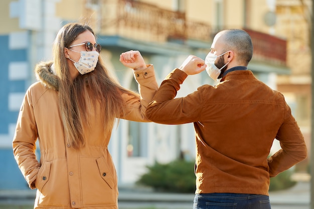 Saludo del codo para evitar la propagación del coronavirus (COVID-19). Un hombre y una mujer con máscaras médicas se encuentran en la calle con las manos desnudas. En lugar de saludar con un abrazo o un apretón de manos, se golpean los codos.
