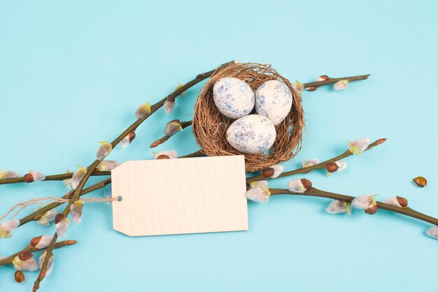 Saludo de Pascua, nido con pequeños huevos de colores, ramas de sauce y una etiqueta en blanco