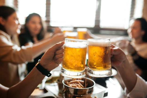 Saludos mano sujetando tazas con cerveza encima de la mesa